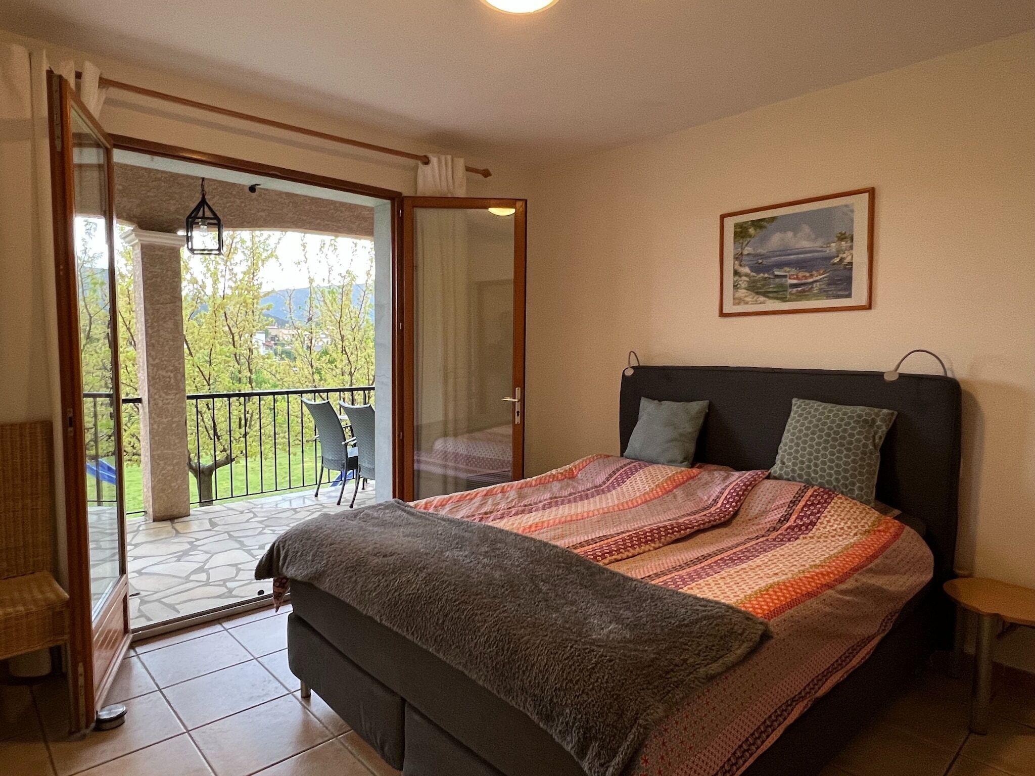 A bedroom with a bed, a balcony, and a painting on the wall.