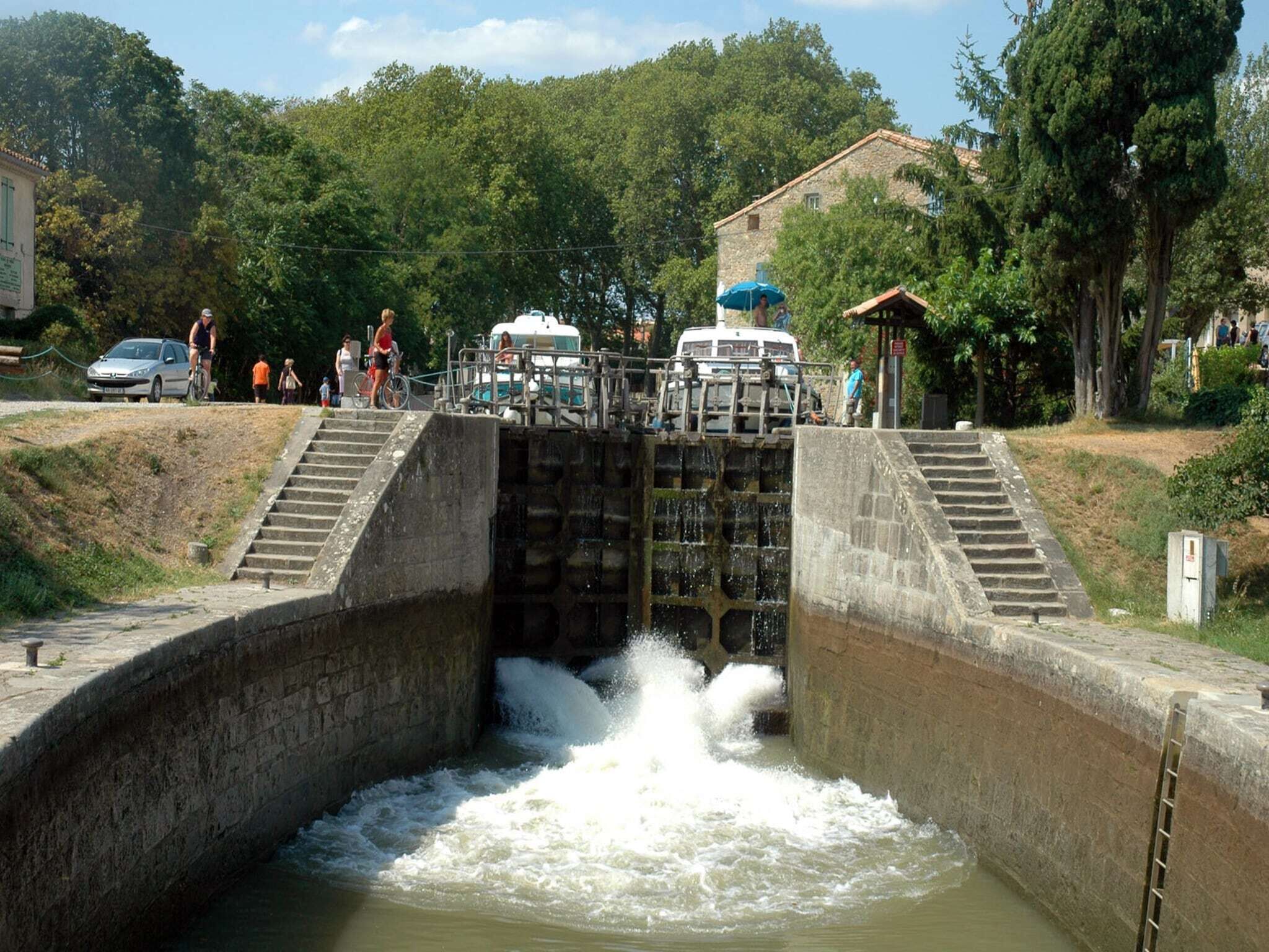 A water lock with steps leading up to it, surrounded by greenery and a building in the background.