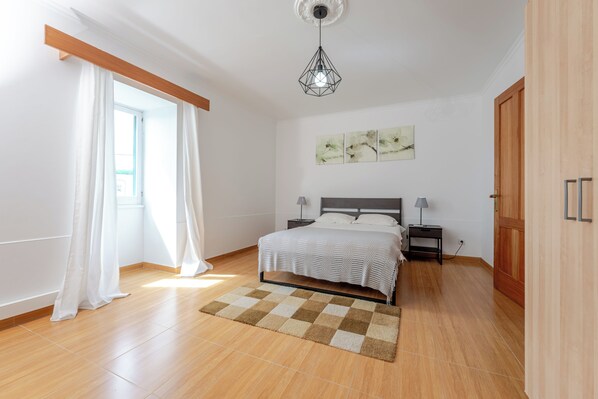 A bedroom with a bed, bedside tables, a lamp, a checkered rug, a ceiling light, and a door.