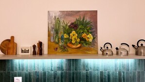 A kitchen counter with a painting, kitchen utensils, and a tiled backsplash.
