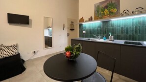 A compact kitchen with a round table, a bowl of fruit, and a green backsplash.