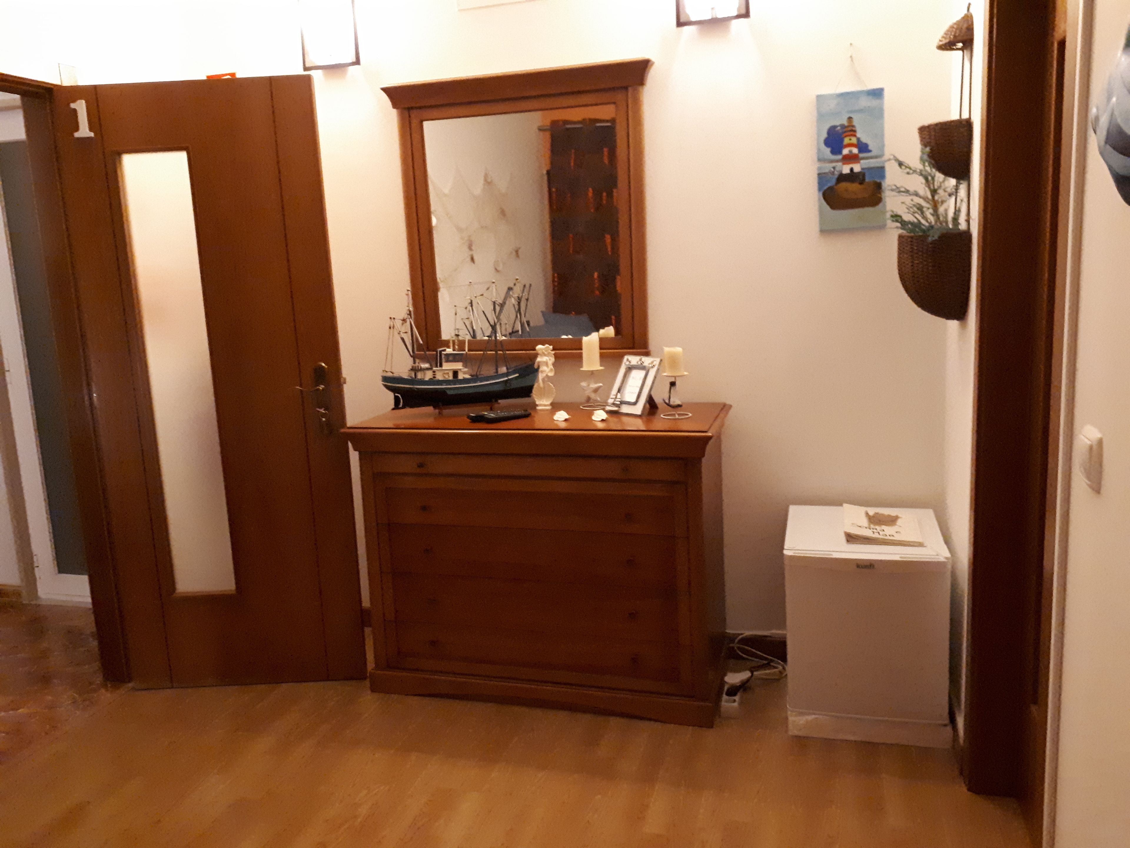 Un comò in legno con uno specchio, un modellino di nave, candele e una cornice con una foto.