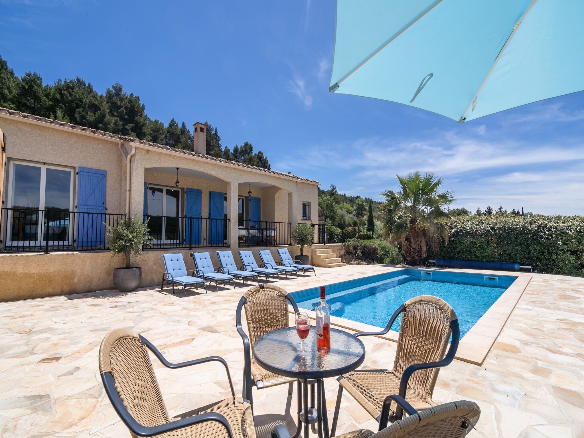 Un espace aménagé au bord de la piscine, avec des chaises longues, une table sur laquelle se trouvent une bouteille et un verre, et un ciel d’un bleu limpide.