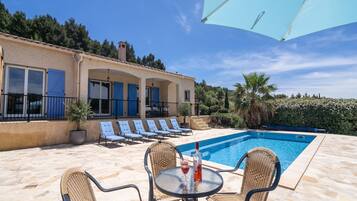 Un espace aménagé au bord de la piscine, avec des chaises longues, une table sur laquelle se trouvent une bouteille et un verre, et un ciel d’un bleu limpide.