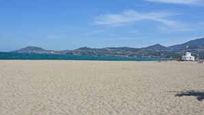 Ein Strand mit einem weißen Gebäude, blauem Himmel und fernen Bergen.
