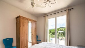 Ein Schlafzimmer mit einem Bett, einem Holzschrank, zwei blauen Stühlen, einem Balkon mit Tisch und Stühlen sowie Blick auf Grün.
