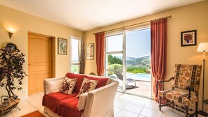 A living room with a sofa, armchairs, a view of the outdoors, and a door leading to a balcony.