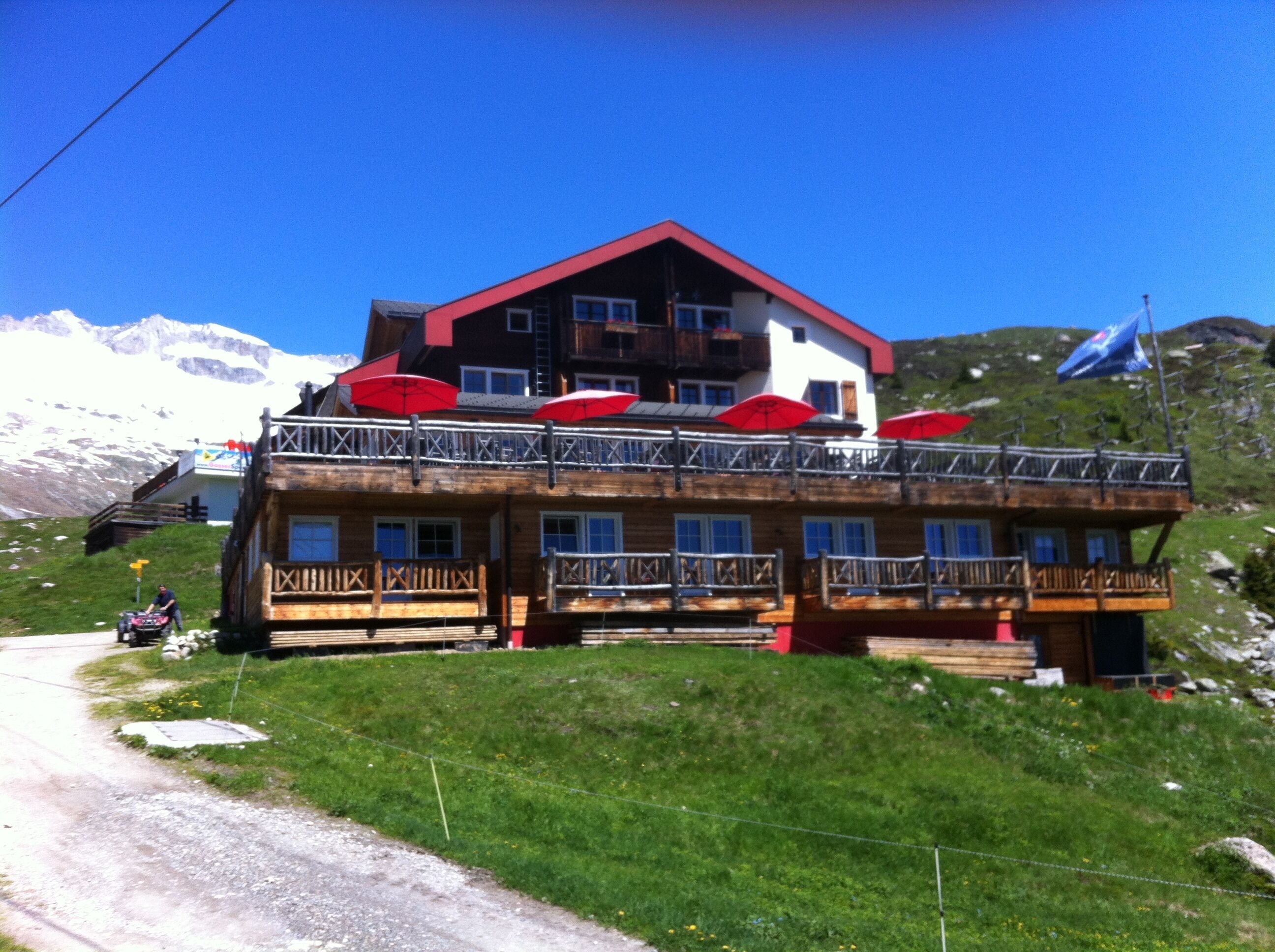 A wooden chalet with balconies and red umbrellas, set against a mountainous backdrop.