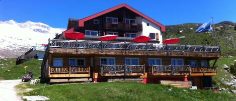A wooden chalet with balconies and red umbrellas, set against a mountainous backdrop.