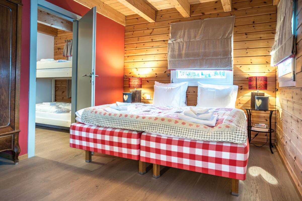 Un dormitorio con una colcha a cuadros, una ventana con cortinas y techo de madera.