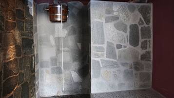 Experience the charm of this cozy bathroom with a stone wall, mosaic-tiled floor, and a wooden bucket.