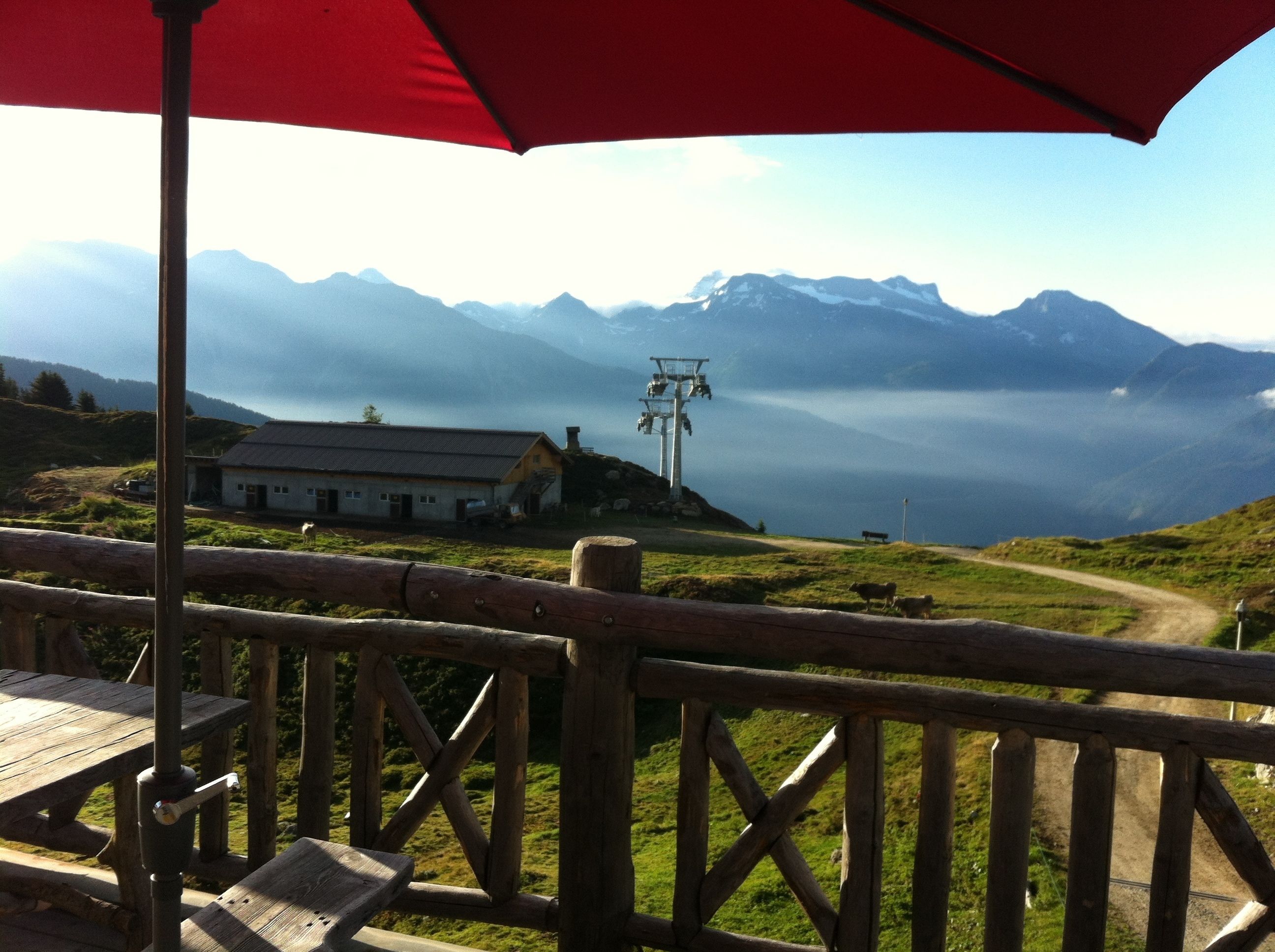 A mountain view with a wooden deck and a red umbrella.