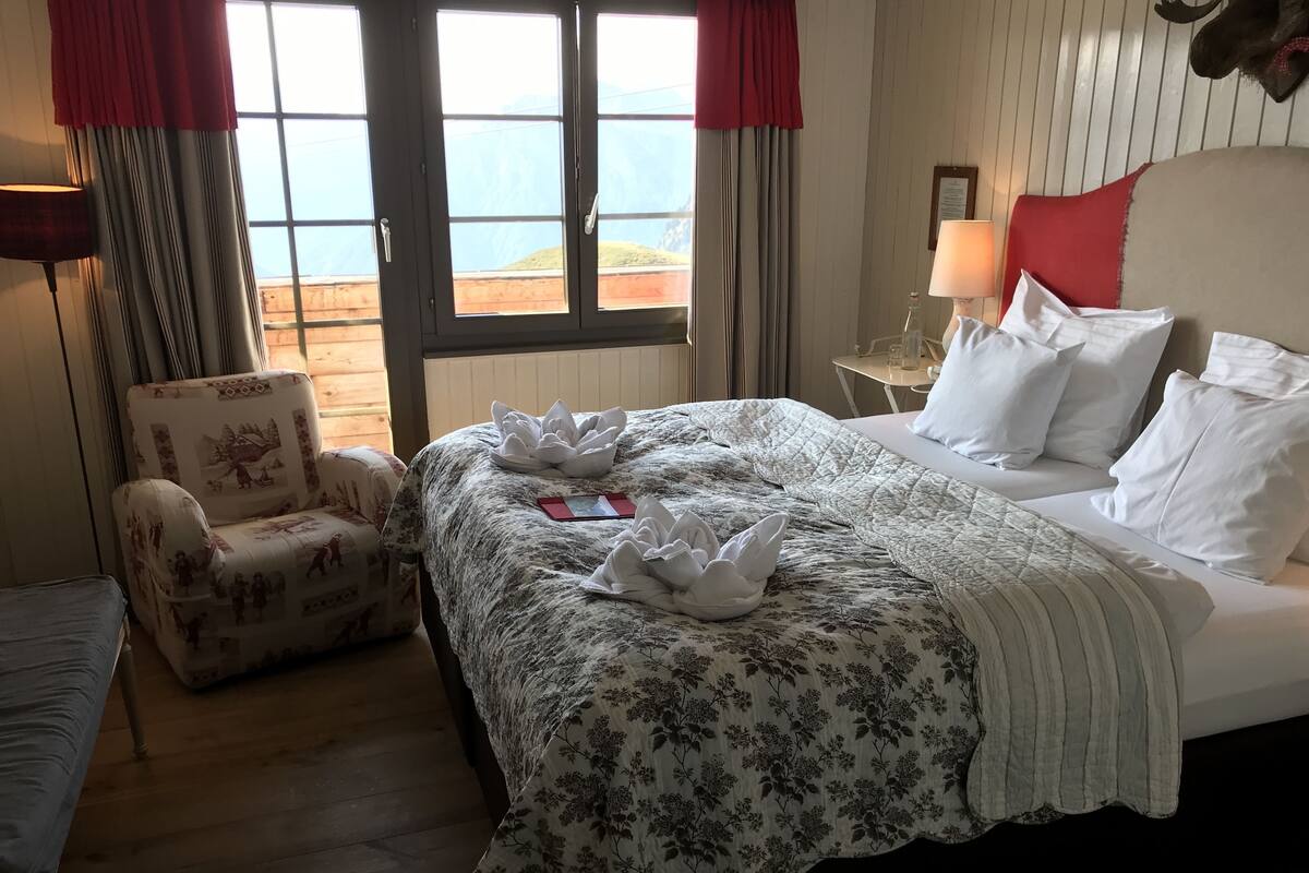 Una habitación de hotel con cama, una silla, una mesa y un ventanal con cortinas.