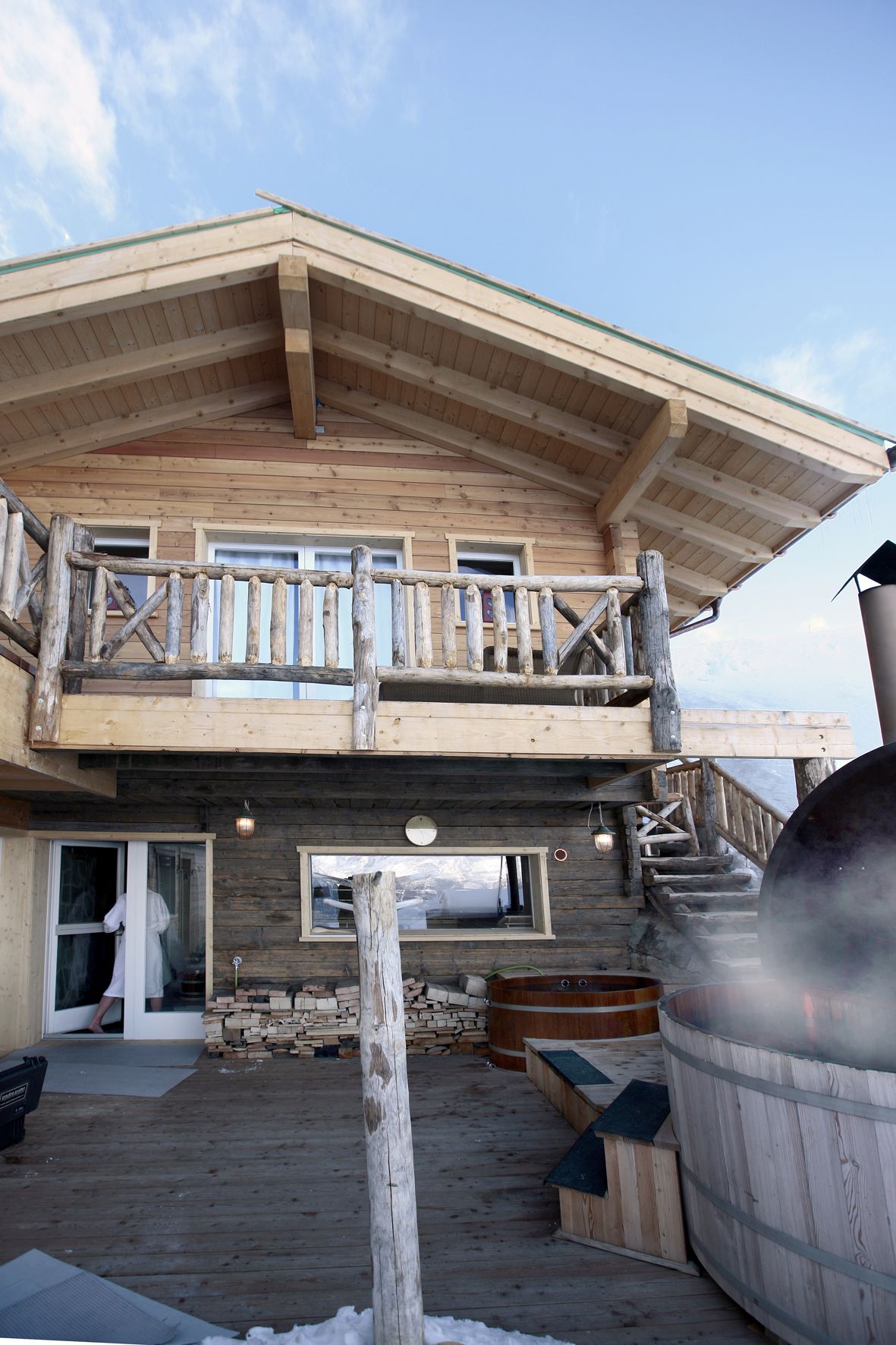 A wooden cabin with a balcony, a hot tub, and a wooden deck.