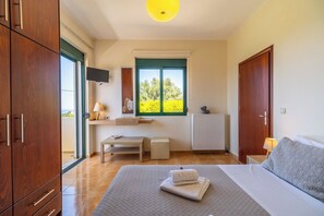 A bedroom with a bed, a desk, a chair, a radiator, and a window with a view of greenery.