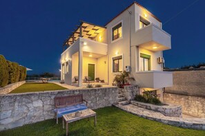 A modern two-story house with a stone retaining wall, a pool, and outdoor seating.