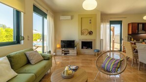 Un salon moderne avec un canapé vert, un téléviseur, une cheminée et un coin repas comprenant une table et des chaises.