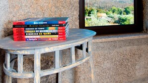 A stack of books on a small table next to a window with a view of a landscape.
