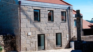 A stone building with a red-tiled roof, three windows, and a stone staircase leading to a door.