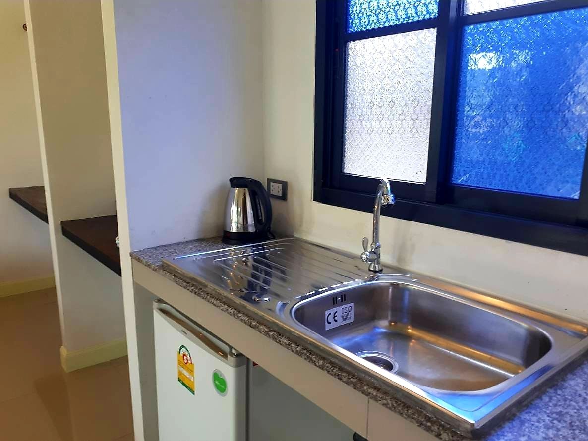 A kitchen with a stainless steel sink, a kettle, and a window with frosted glass.
