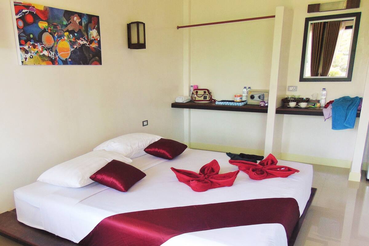 A neatly made bed with white and red linens, a bedside table with a lamp, and a painting on the wall.