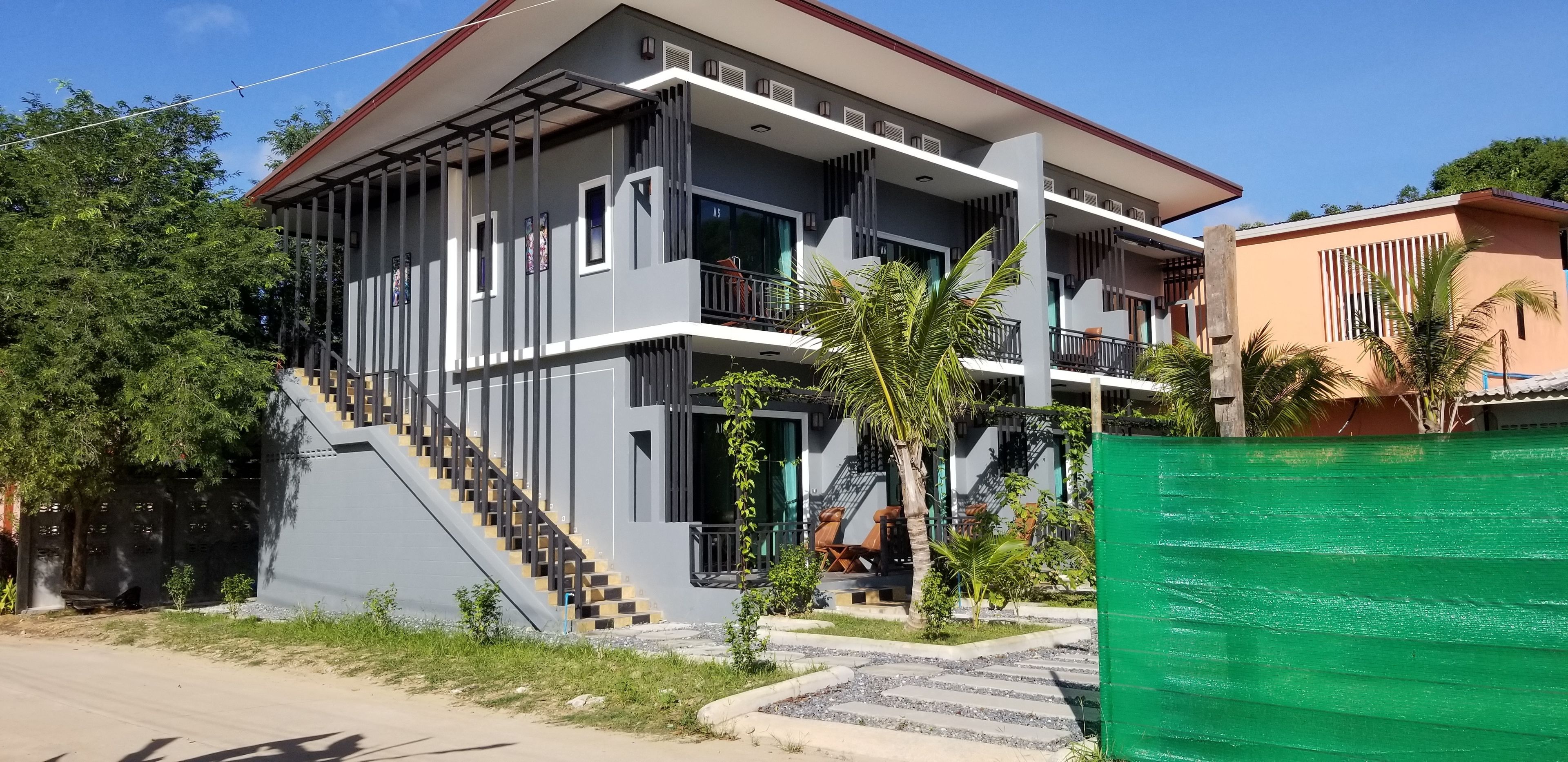 Un edificio de varios pisos con una escalera que conduce a los pisos superiores, balcones y una cerca verde al frente.