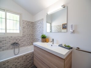 A modern bathroom with a bathtub, a sink with a mirror, and a window. - Beautiful villa with private heated pool (Roquebrun)