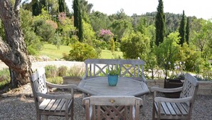 An outdoor seating area with a wooden table and chairs, surrounded by gravel, with a view of a lush garden and trees in the background. - Relaxing Retreat Near Minerve (Cesseras)