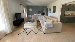 A living room with a beige sofa, a coffee table, and a TV. There is a kitchen area with cabinets and a countertop. - Relaxing Retreat Near Minerve (Cesseras)