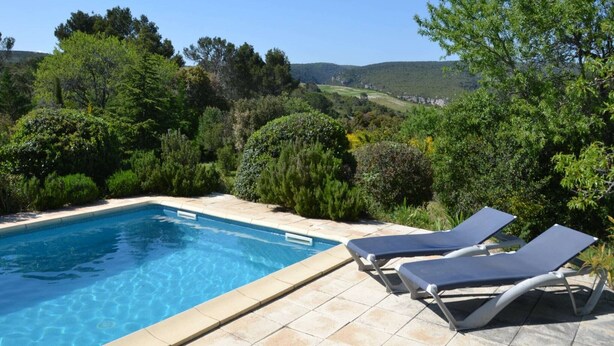 A swimming pool with two lounge chairs, surrounded by lush greenery and a hilly landscape in the background. - Relaxing Retreat Near Minerve (Cesseras)
