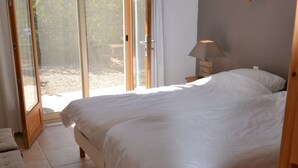 A bedroom with a large bed, a wooden nightstand, a lamp, and a sliding glass door leading to an outdoor area. - Relaxing Retreat Near Minerve (Cesseras)