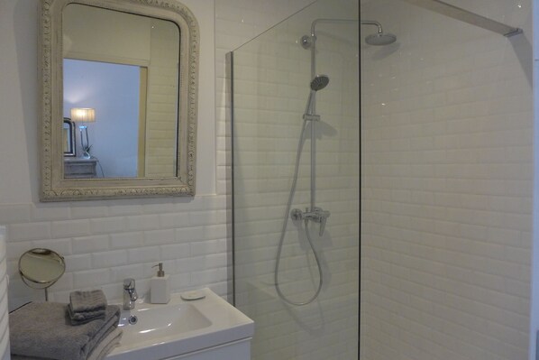 A bathroom with a glass-enclosed shower, a sink with a mirror, and a towel rack. - Blumereve (Blumeray)