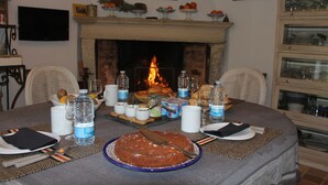 Una mesa de comedor preparada para una comida, con un pastel, botellas de agua y una chimenea al fondo.