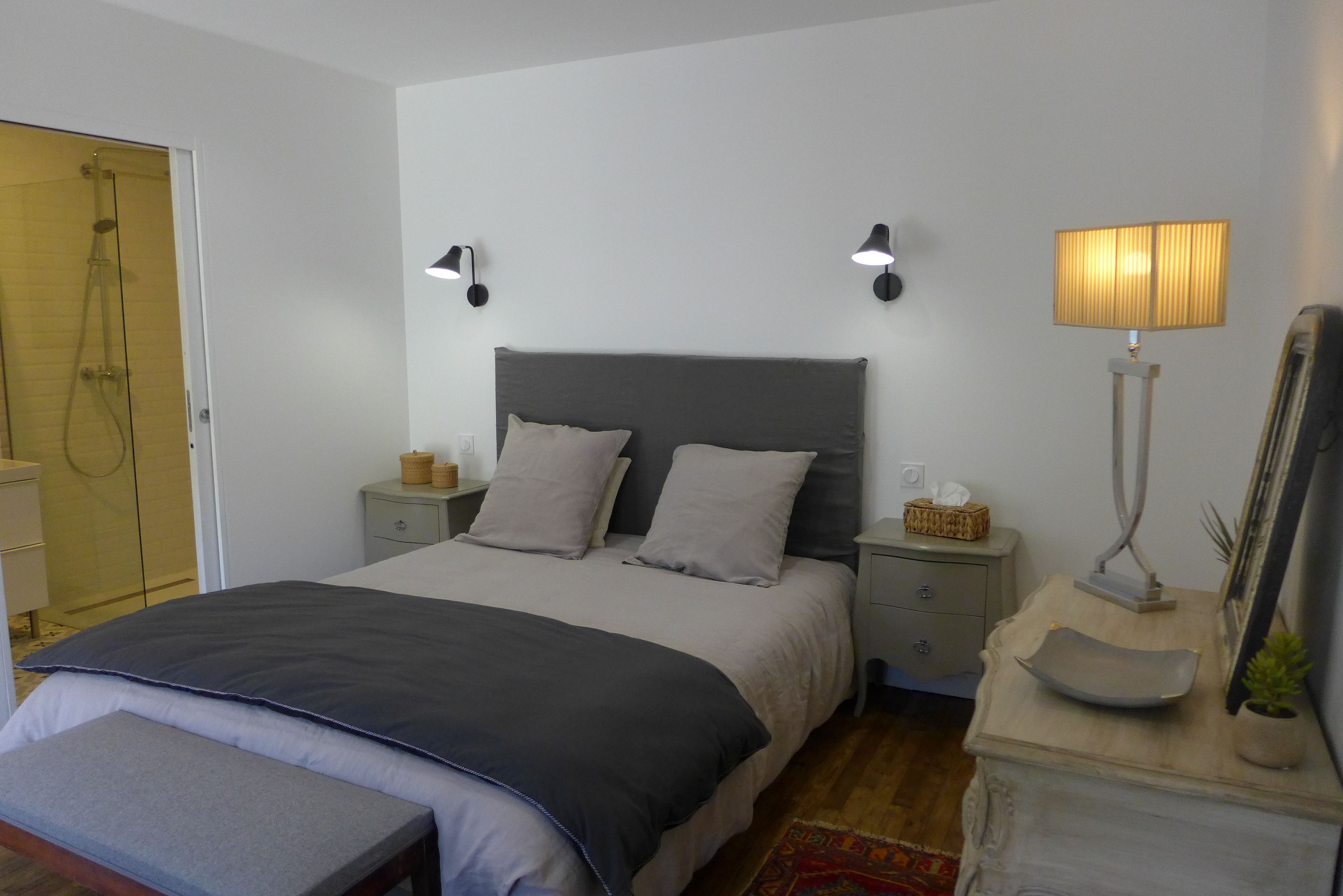 A bedroom with a bed, bedside tables, a lamp, and a shower area.