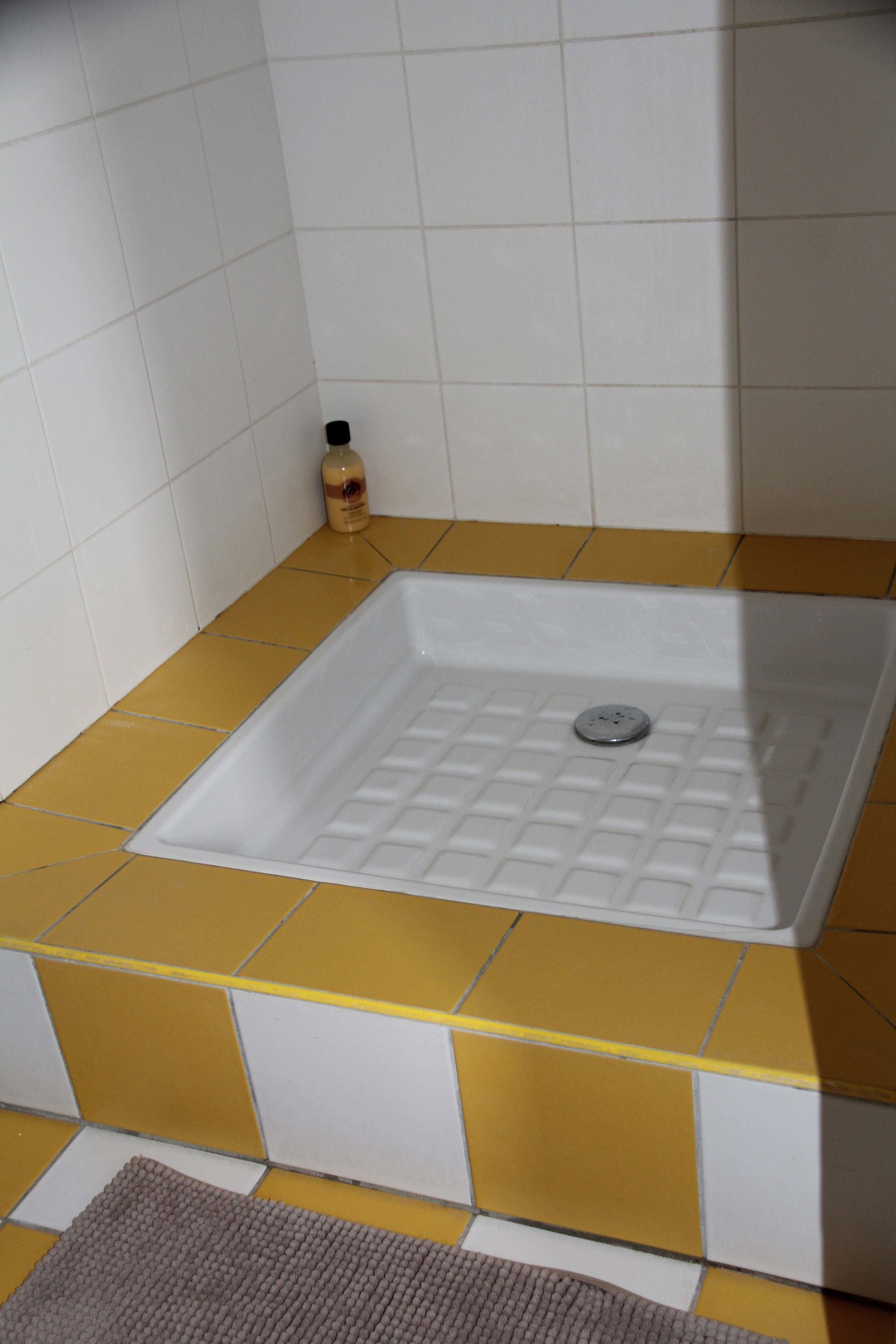 A bathroom with a white bathtub, yellow and white tiled floor, and a small bottle of soap on the counter.