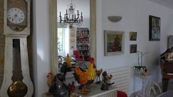 A room with a large mirror reflecting a chandelier, a clock, and a bookshelf filled with books and decorative items.