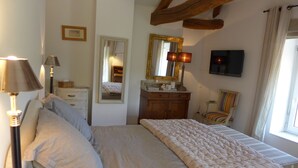 Un dormitorio con cama, lámparas de noche, cómoda, espejo, televisor y ventana con cortinas.