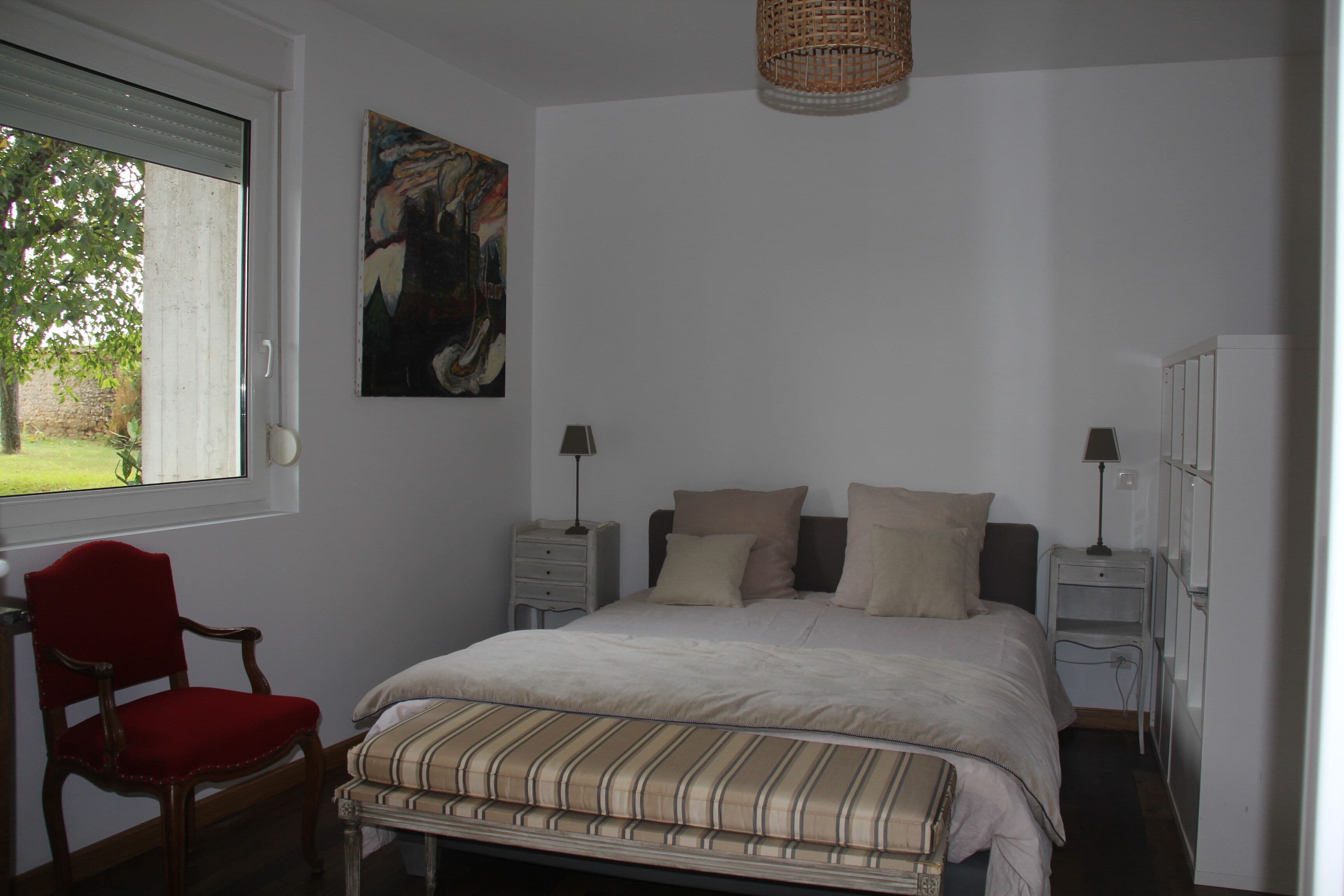 A bedroom with a bed, two bedside tables, a chair, a painting, and a window.