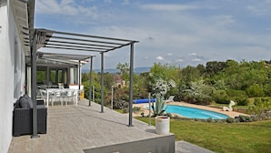 A covered outdoor area with a pool, a patio with chairs, and a view of the surrounding landscape. - Villa in Malves near Carcassonne Pool (Malves en Minervois)