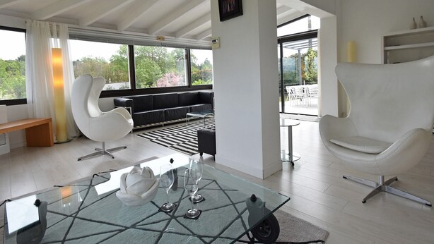 A modern living room with a glass coffee table, white leather armchairs, a black sofa, and a view of the outdoors through large windows. - Villa in Malves near Carcassonne Pool (Malves en Minervois)