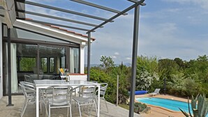 A modern outdoor dining area with a glass table and chairs, a pergola, and a pool in the background. - Villa in Malves near Carcassonne Pool (Malves en Minervois)