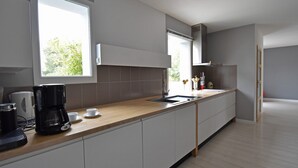 A modern kitchen with a wooden countertop, white cabinets, a coffee maker, and a window providing natural light. - Villa in Malves near Carcassonne Pool (Malves en Minervois)