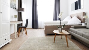 Een moderne hotelkamer met een bed, bank, bureau, stoel en een kleine tafel met een plant.