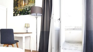 Een kamer met een bureau, stoel, vloerlamp en een openslaande balkondeur.