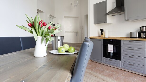 Een moderne keuken met grijze kastjes, een houten aanrecht en een eettafel met een vaas tulpen en appels.