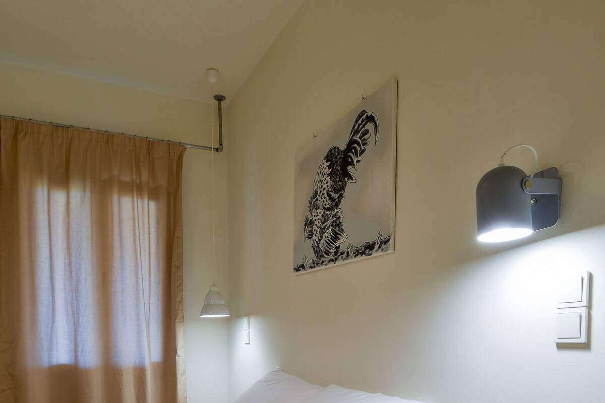 A single bed with white bedding, a wooden nightstand, a wall-mounted light, and a framed artwork.