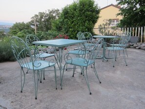 An outdoor patio with metal tables and chairs, surrounded by greenery and a view of a distant landscape. - Nada Apartments (Opatija)