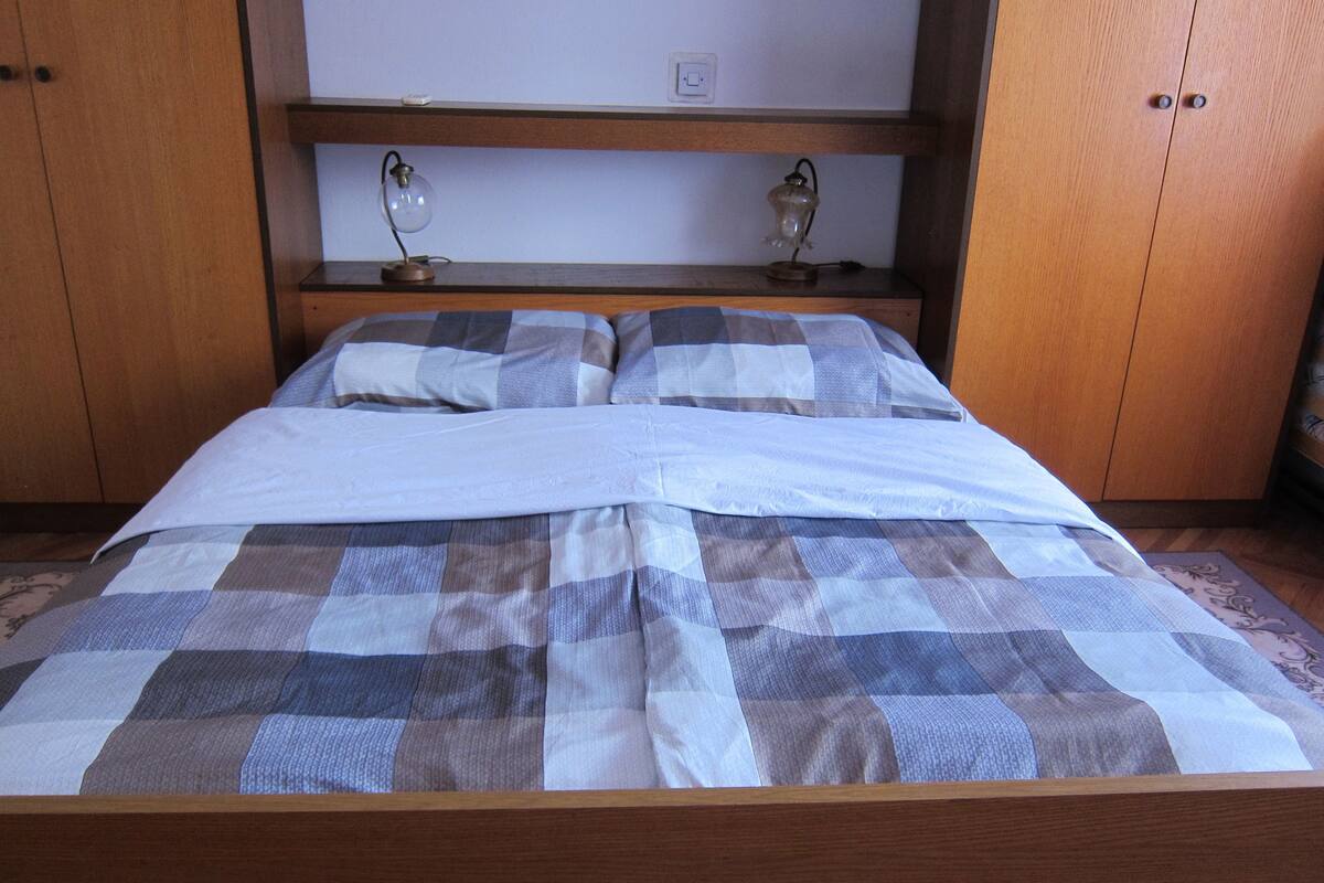 A bed with a checkered bedspread, wooden headboard, and two bedside lamps.