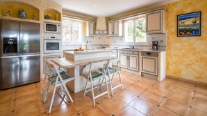 A modern kitchen with a central island, stainless steel appliances, and a large window providing natural light. - Hillside Retreat in Roquebrun (Roquebrun)