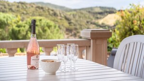 A table with a bottle of wine, a bowl of nuts, and wine glasses on a terrace with a scenic mountain view. - Hillside Retreat in Roquebrun (Roquebrun)